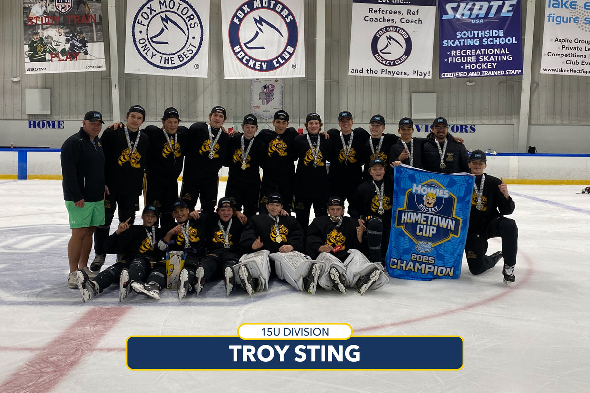 Ice hockey team posing with championship banner on an ice rink, surrounded by event banners.