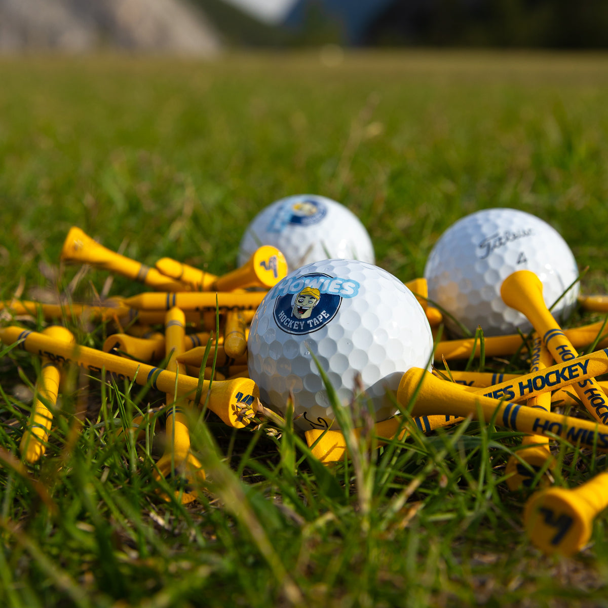 Golf balls with yellow tees on grass with mountains in the background