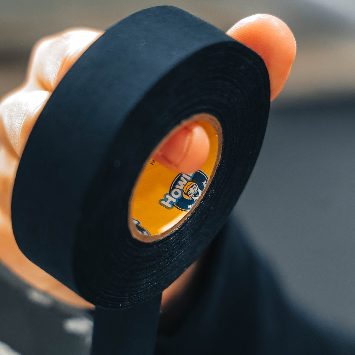 Person holding a roll of black tape with a visible brand logo.