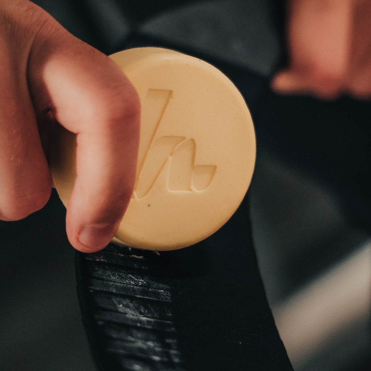 hand applying howies tacky wax to a hockey blade with black howies cloth tape on it