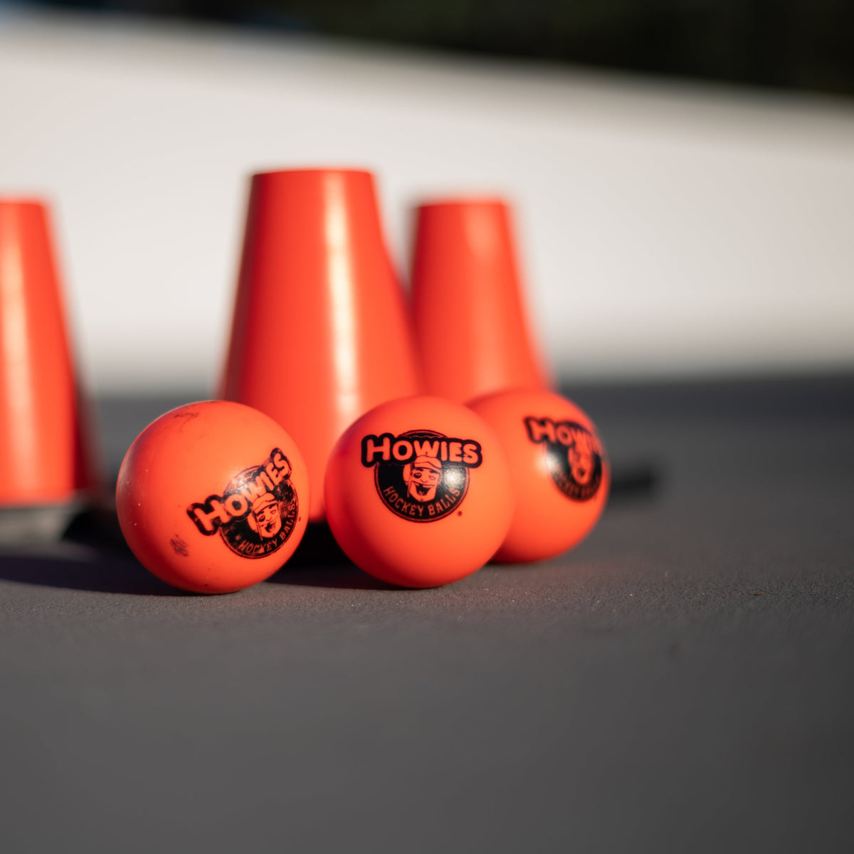 Three orange hockey pucks with 'Howies' branding on a gray surface.