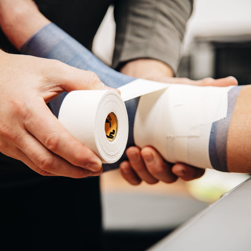 Person applying tape to a person's arm with a focus on the hands and tape.