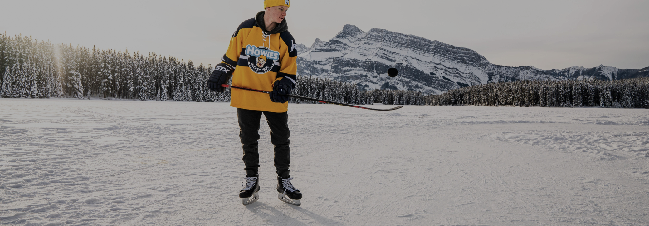 Person ice skating on a frozen lake with snow-covered mountains in the background