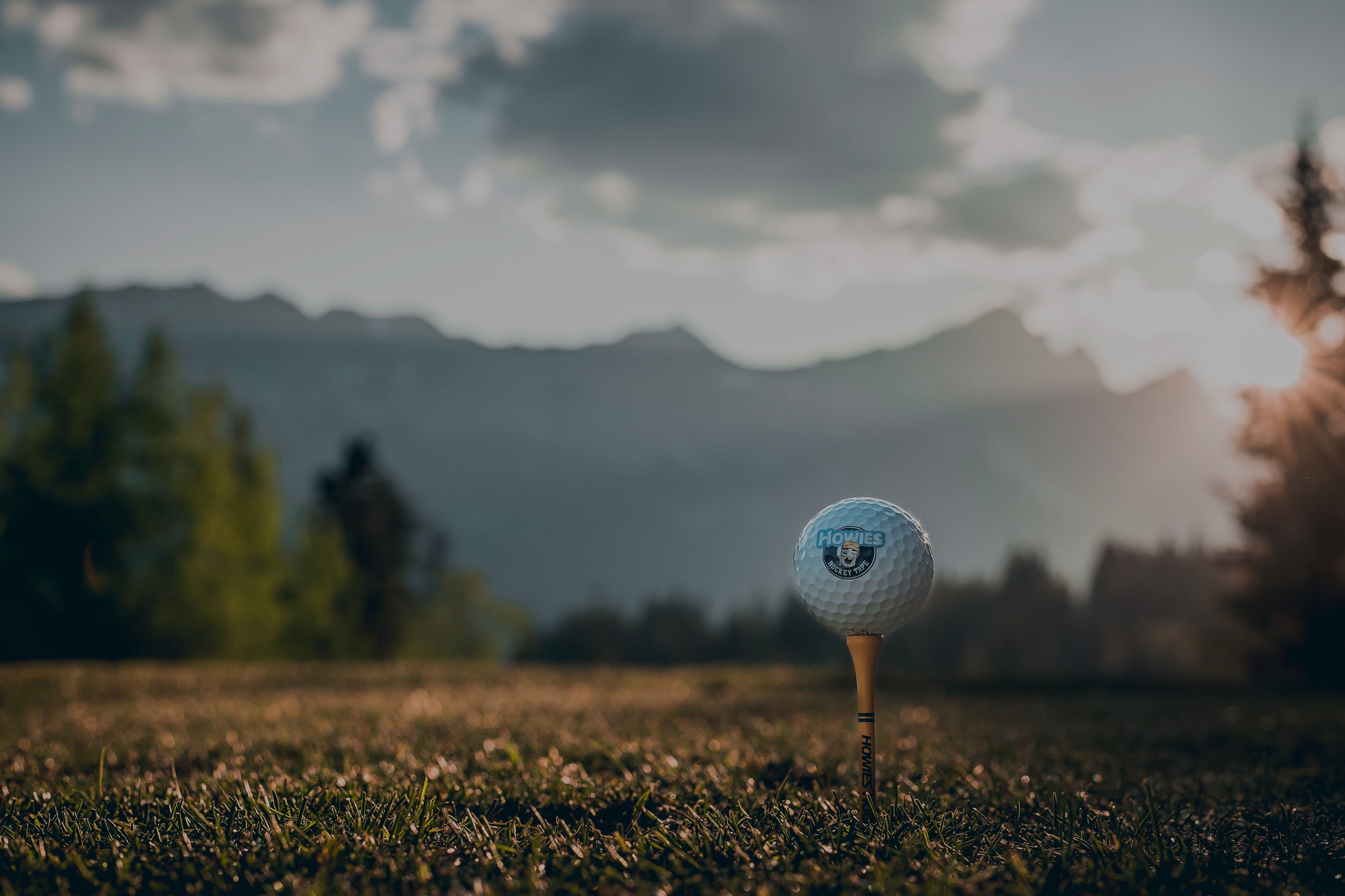 Golf ball on a tee with a scenic background of mountains and trees.