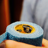 Roll of blue tape with a yellow label featuring the 'Howies' logo, held by a person.