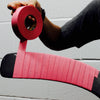 Person applying pink tape to a hockey stick against a white wall