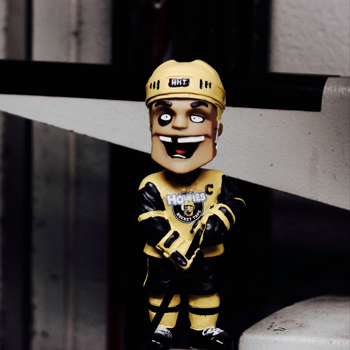Bobblehead figure in a black and gold sports uniform with a helmet, sitting on a surface.