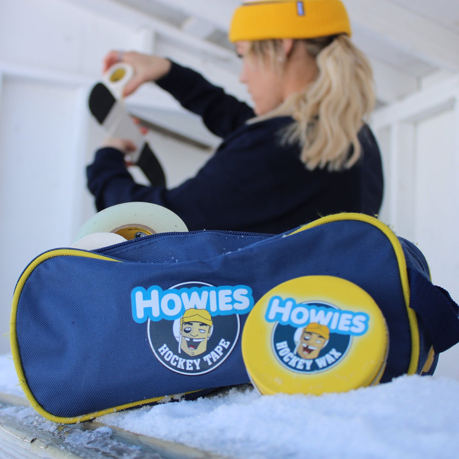 Person sitting on a snowbank with a Howies hockey bag and equipment