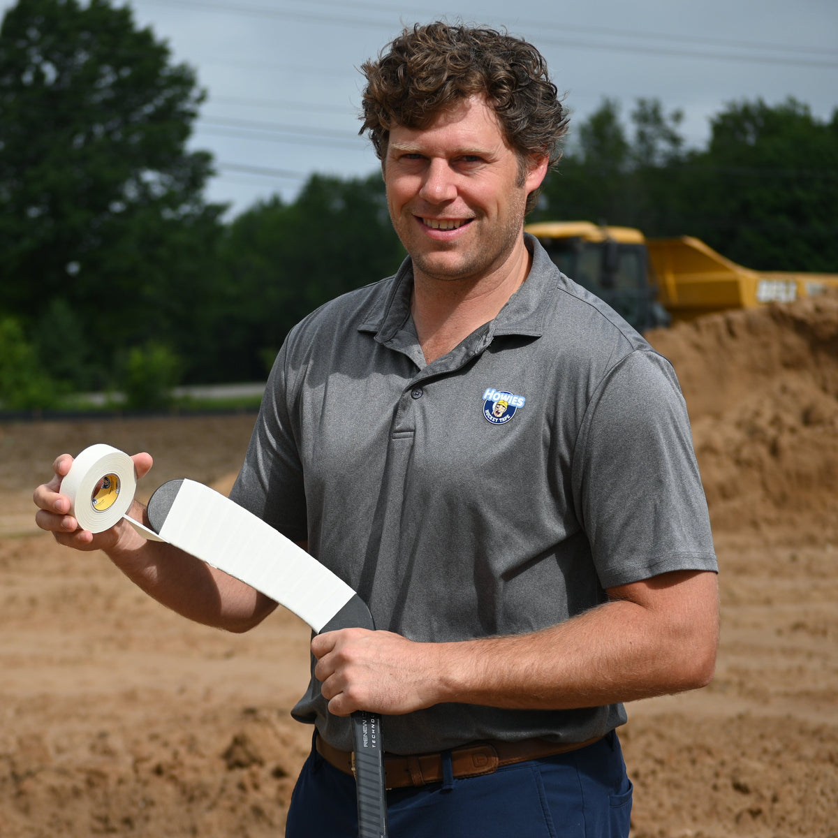 Man holding a roll of tape in an outdoor setting with construction equipment in the background