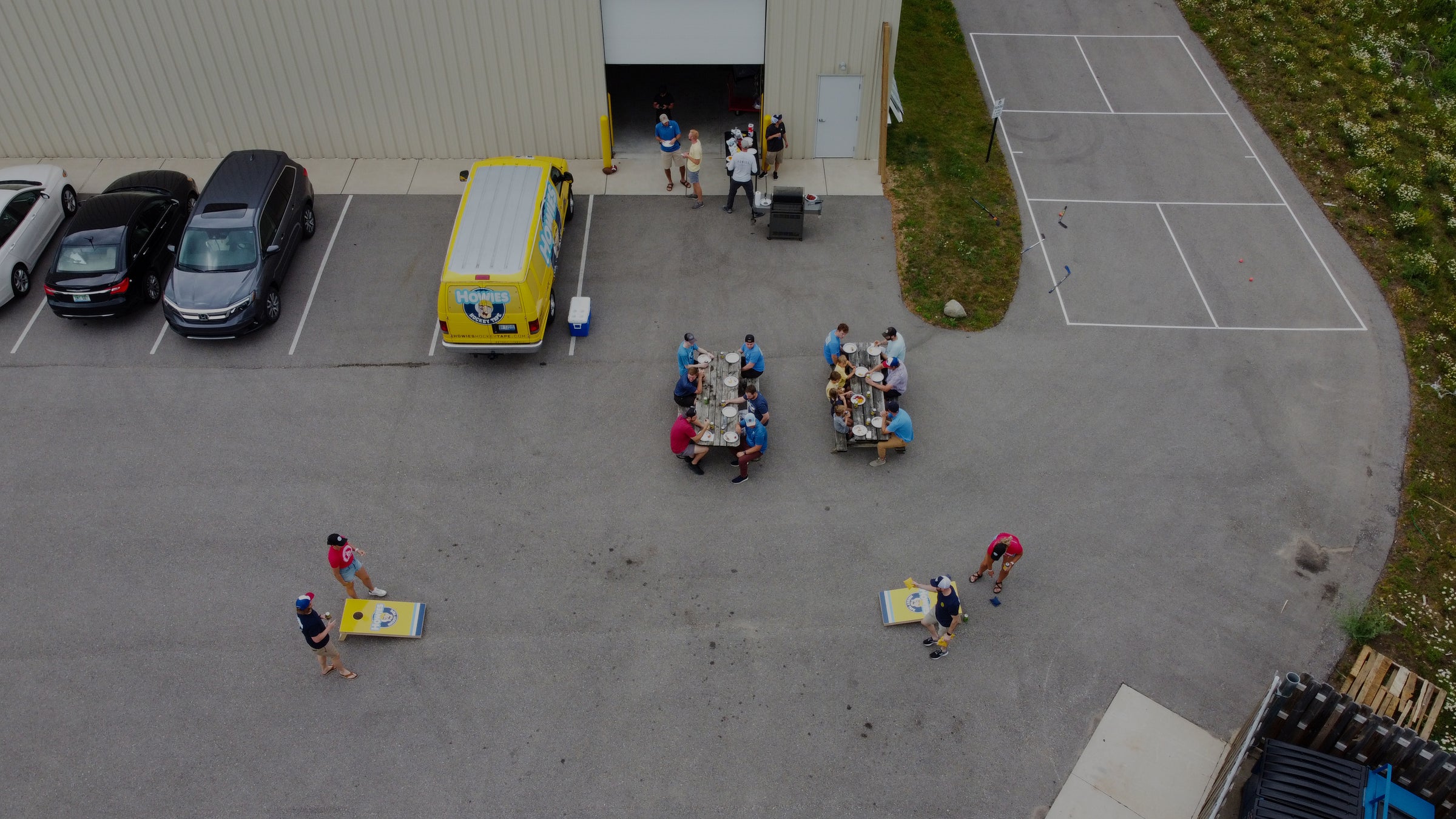 Aerial view of a parking lot with people and vehicles, including a yellow truck and a building in the background.