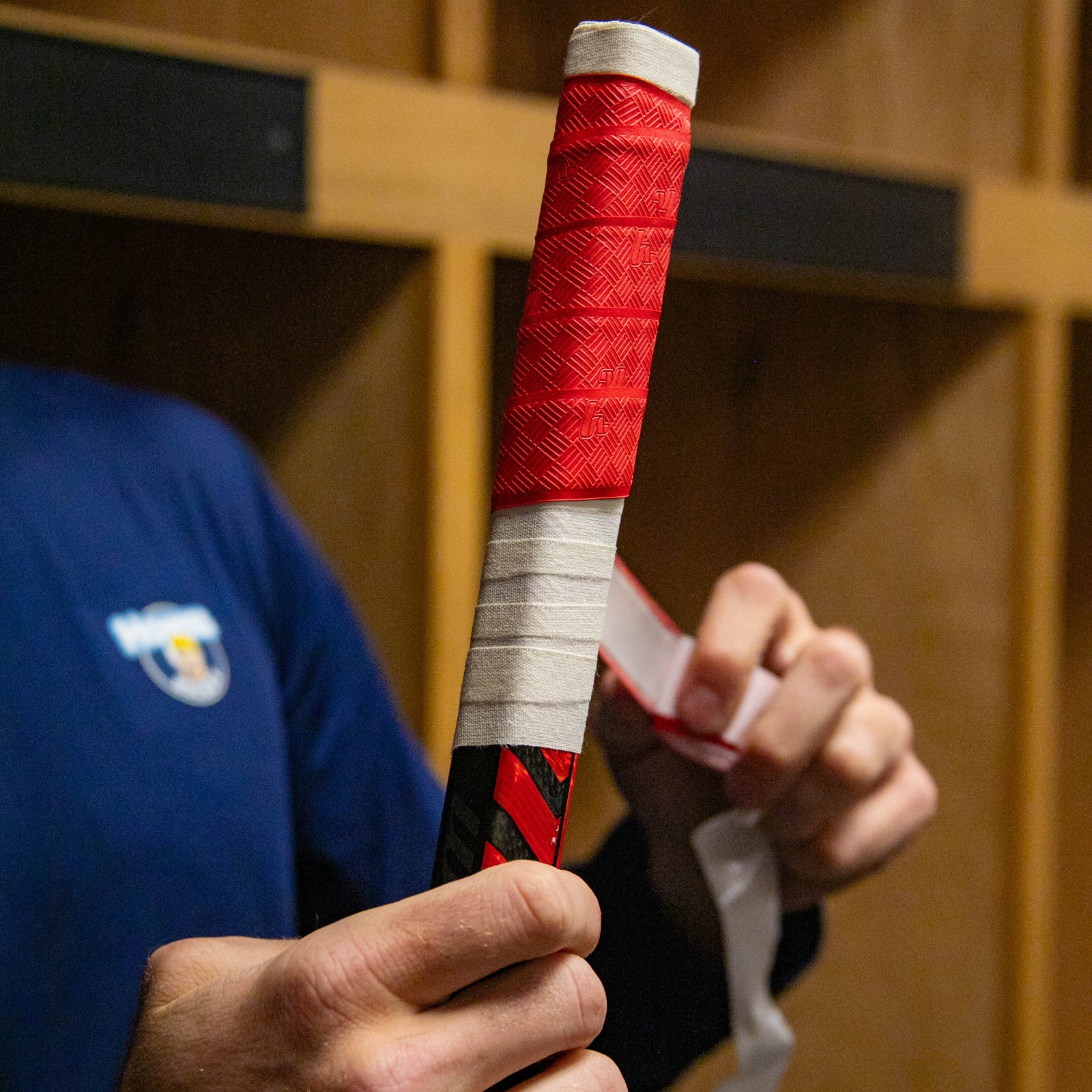 Person holding a hockey stick with red and white tape in a locker room.