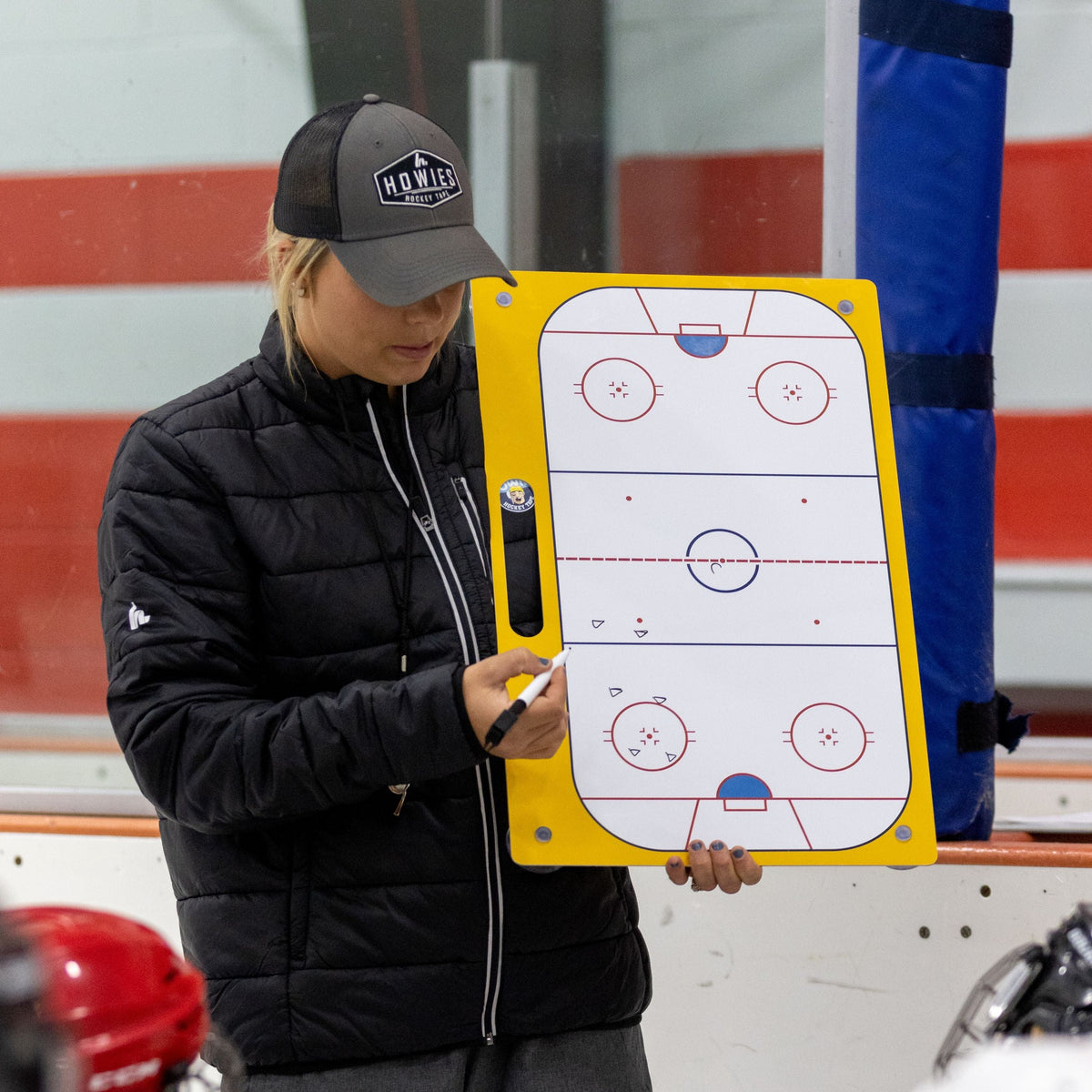 Person holding a hockey tactics board with children on an ice rink