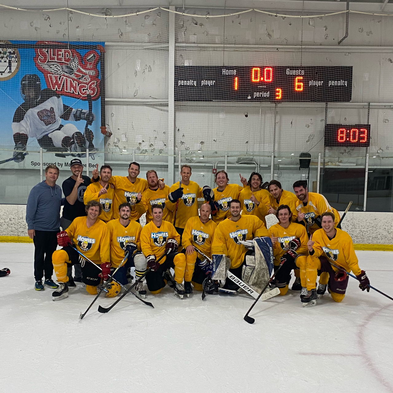 Hockey team posing on the ice with a scoreboard in the background