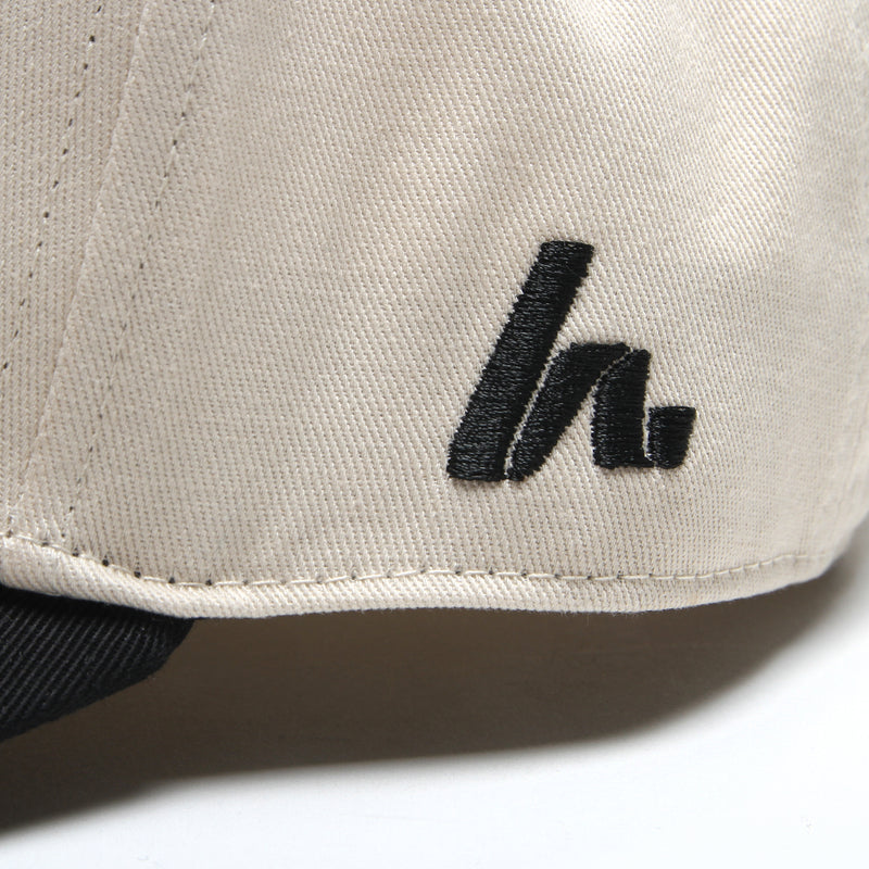 Close-up of the black embroidered Howies "h" logo on the side panel of the cream Clean Sheet Lid